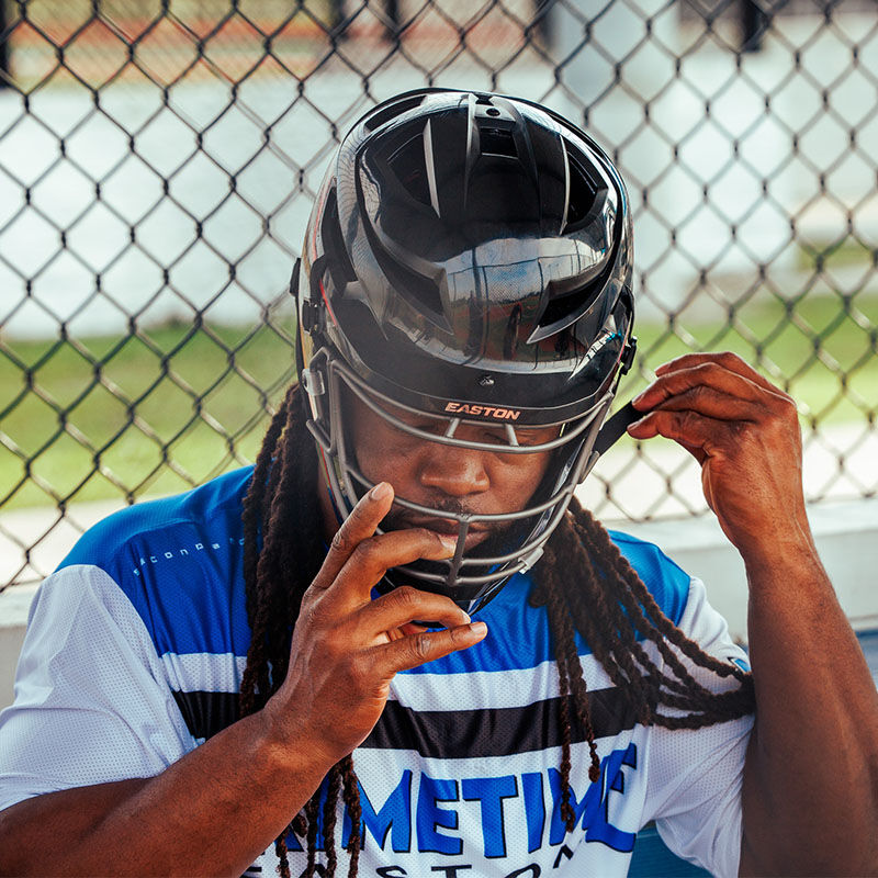 A player in a dugout securing the chin strap clips on his Hellcat Mojo helmet - SKU: HELMOSPH loading=
