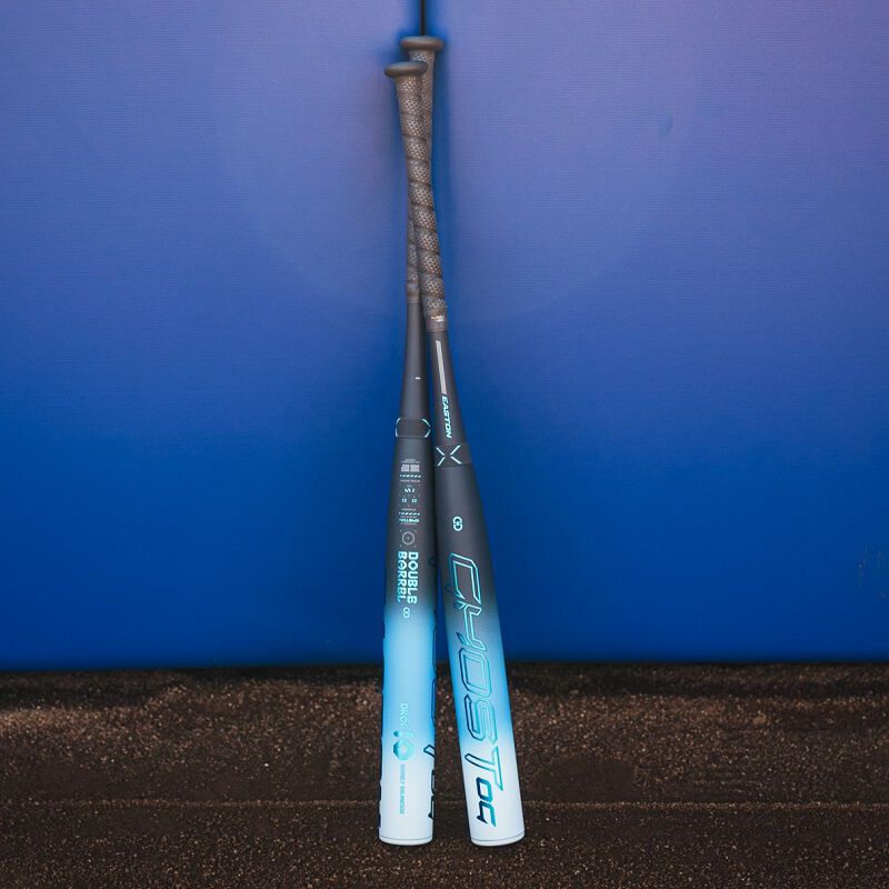 A picture of two 2025 Easton Ghost OG fastpitch bats leaned against a blue backstop