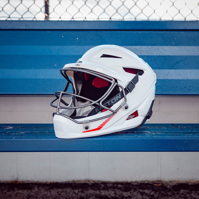 A white Easton Hellcat slowpitch fielding helmet sitting on a dugout bench - SKU: EHCATH