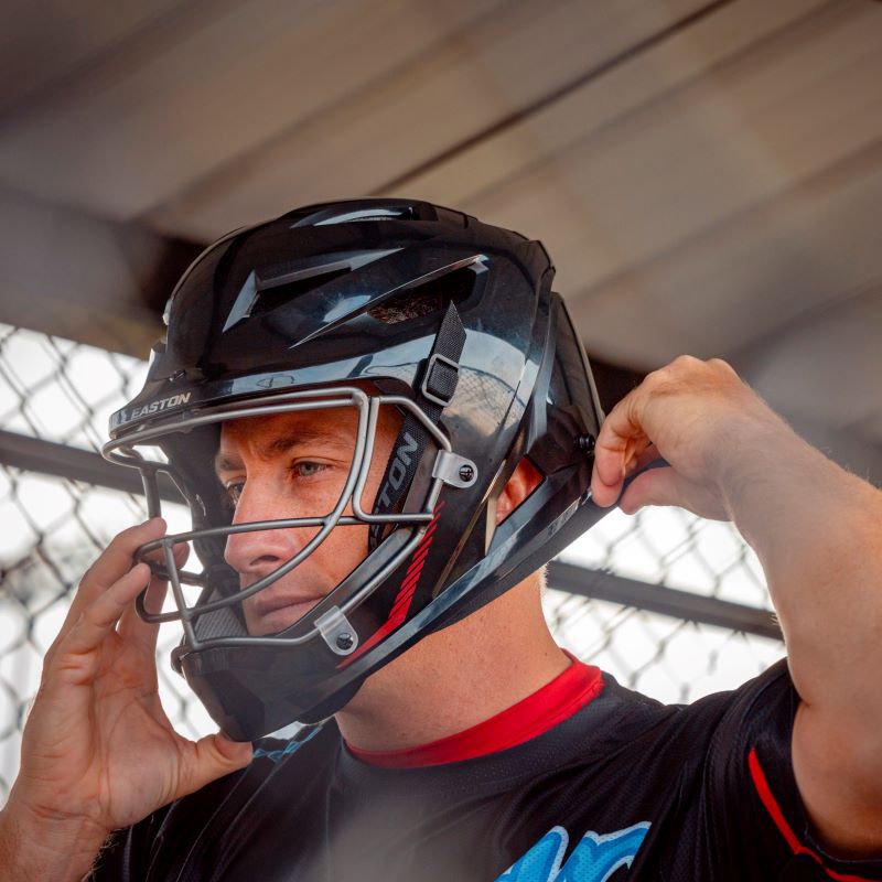 A player clipping on the straps for his black Hellcat slowpitch fielding helmet - SKU: EHCTAH loading=