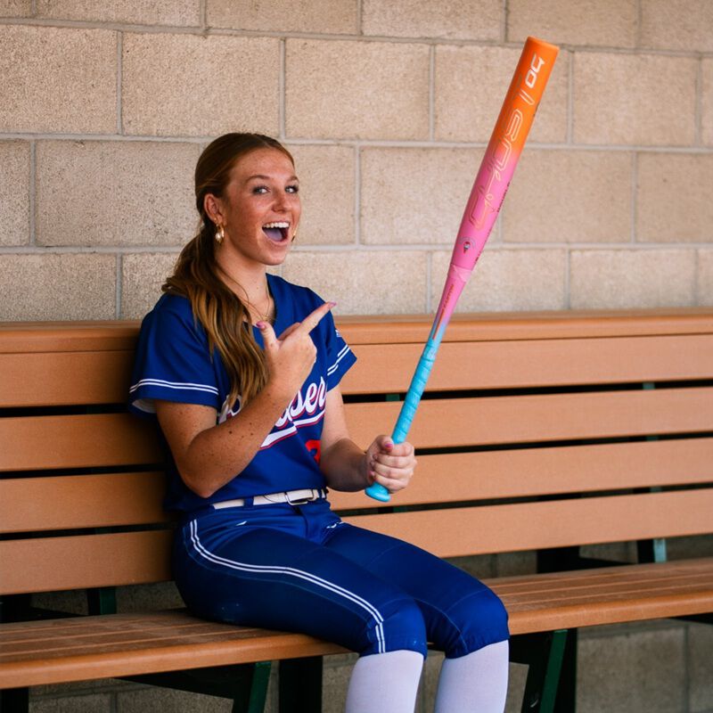 Picture of a player sitting on a bench with an Easton Ghost OG Rainbow sherbet fastpitch bat
