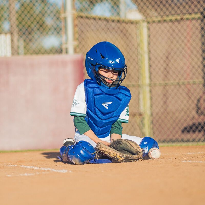 A player blocking a ball wearing a royal Easton Black Magic 3.0 youth catcher's set