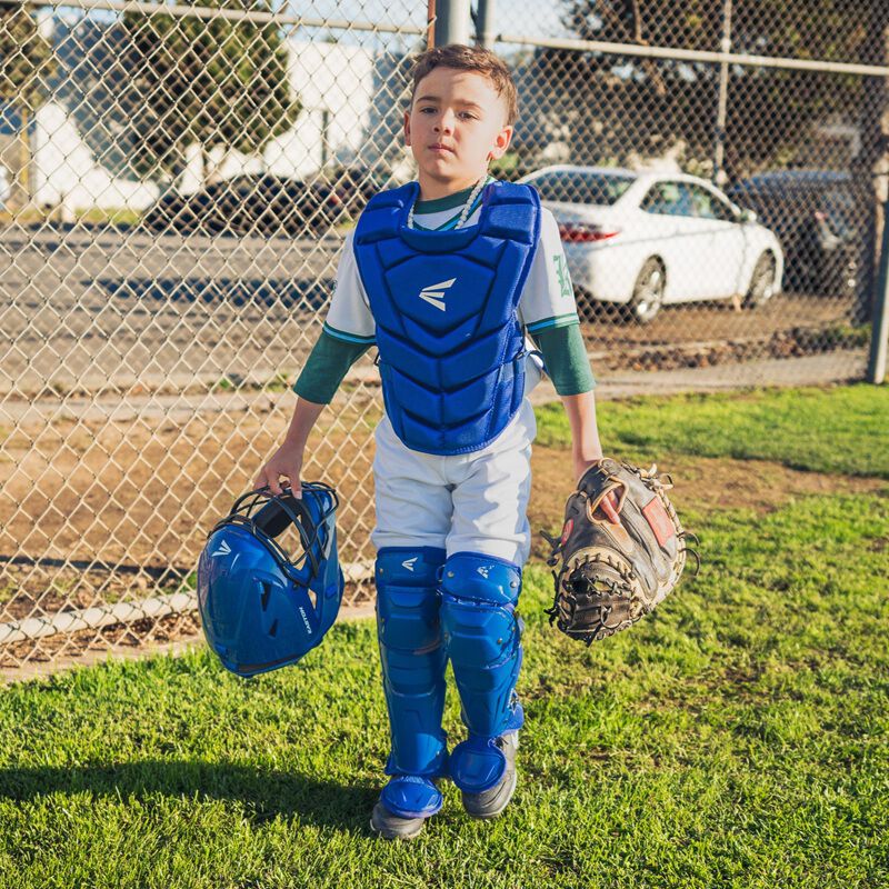 A player wearing royal Easton Black Magic 3.0 youth catcher's set holding the helmet 