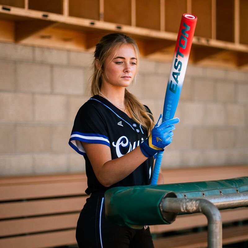 A player holding a red/white/blue Easton Ghost OG Rocket Pop fastpitch bat