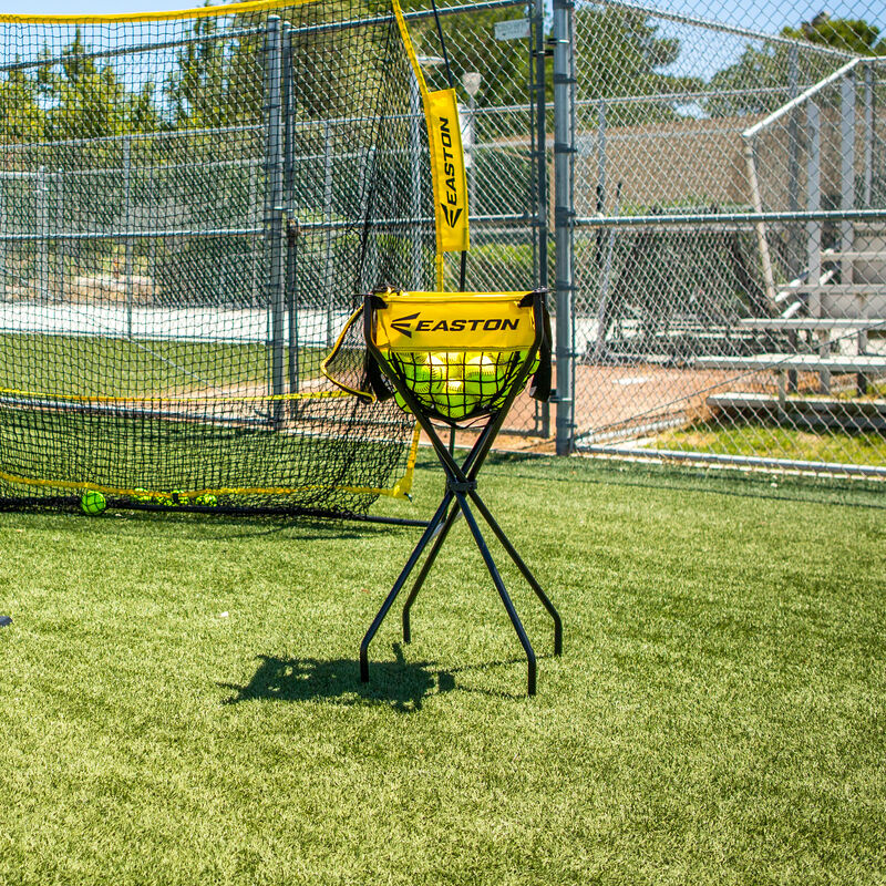 A picture of an Easton Ball Caddy with softballs on a field in front of a training net loading=