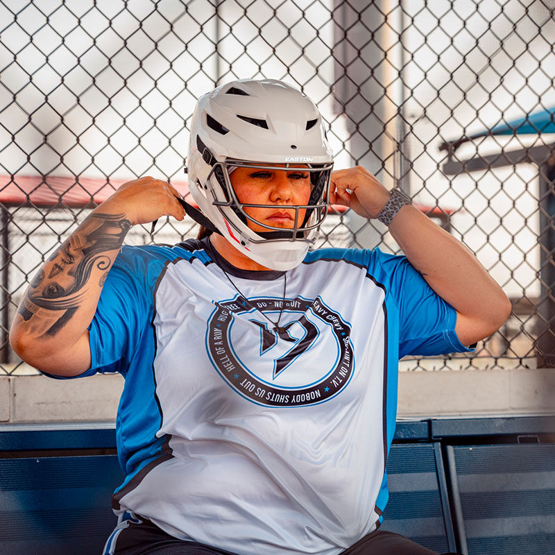 A female player strapping on a white Hellcat slowpitch fielding helmet - SKU: EHCATH loading=