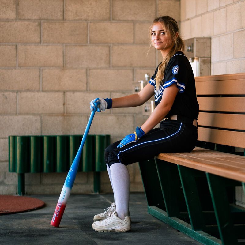 A player sitting on a bench with a red/white/blue Easton Ghost OG Rocket Pop fastpitch bat