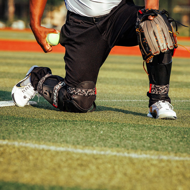 A pitcher down on one knee wearing a pair of Hellcat Mojo leg guards - SKU: HELMOLG loading=
