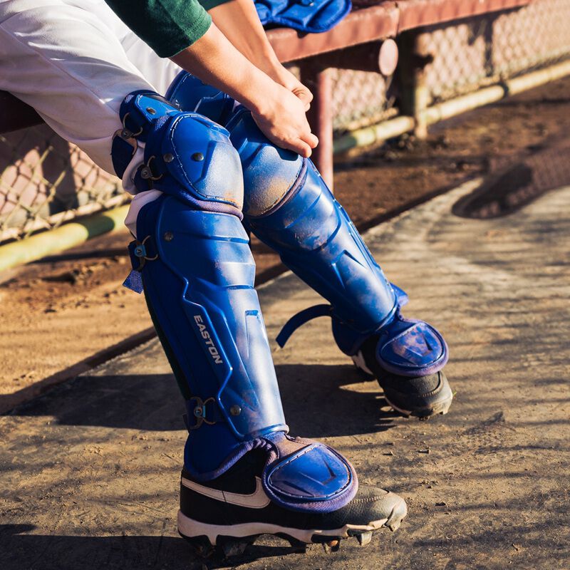 Picture of a player putting on royal Easton Black Magic 3.0 youth leg guards