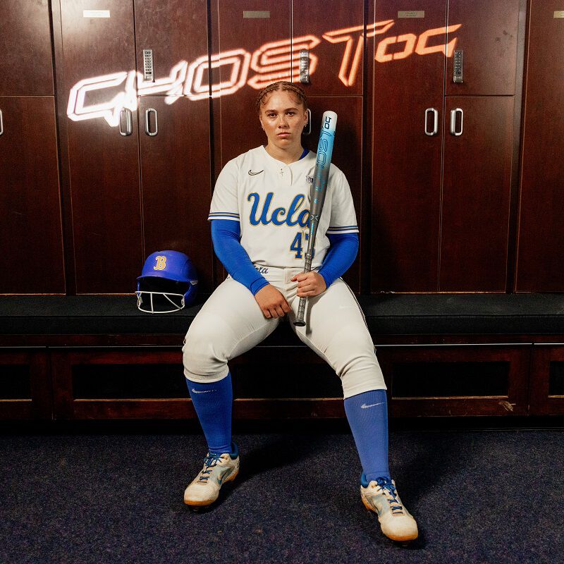 Picture of a UCLA fastpitch player sitting in a locker room with a 2025 Easton Ghost OG fastpitch bat and the "Ghost OG" logo above her