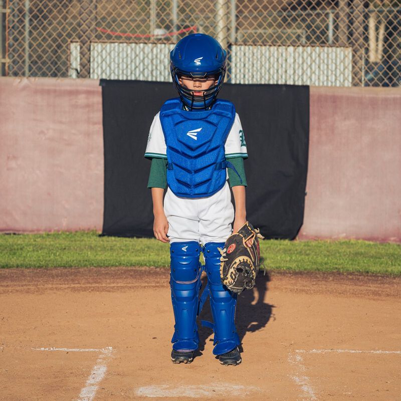 A player standing behind home plate wearing royal Easton Black Magic 3.0 youth catcher's set