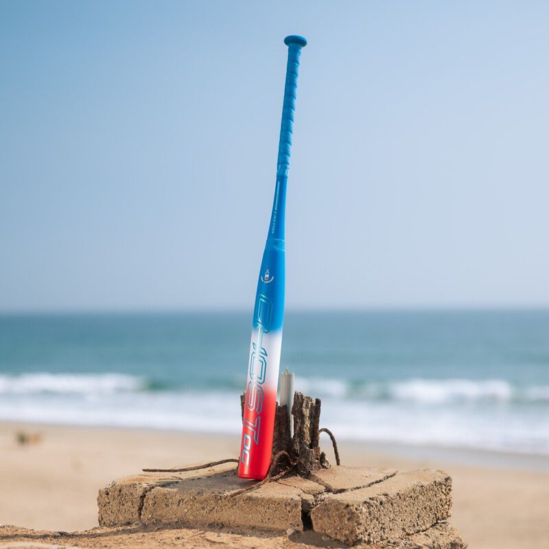 A red/white/blue Easton Ghost OG Rocket Pop fastpitch bat standing on its end on a beach