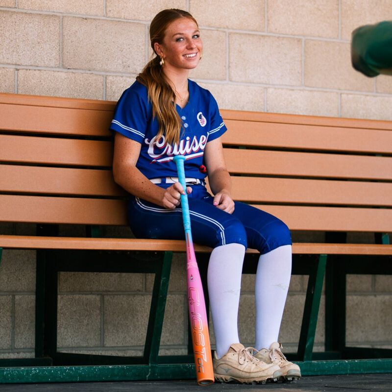 Picture of a player with an Easton Ghost OG Rainbow sherbet fastpitch bat on the bench in a dugout loading=